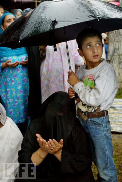 A young child holds an umbrella as Kashmiri Muslim pilgrims pray in the rain in Srinagar, Kashmir.