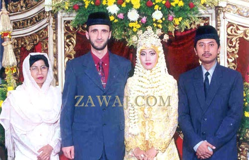 The couple together on the pelaminan or bridal dais, along with the bride's mother and brother.